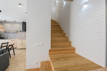 modern interior shows a living area with light wood stairs, white brick walls, a gray sofa, and a...