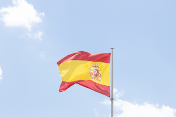 Vibrant flag of Spain waving against a clear blue sky, showcasing rich colors and intricate design, symbolizing national pride and cultural identity in a sunny atmosphere