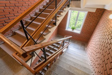 Staircase with brick walls and wooden handrails. A window with a plant sits on the landing.