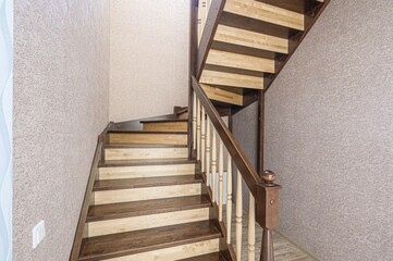 wooden staircase with brown-stained treads and light wood risers leads upwards. The walls are textured.