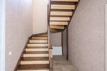 wooden staircase with brown-stained treads and light wood risers leads upwards. The walls are textured.