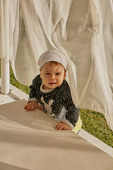 Little baby girl is playing behind the white curtains outdoors.