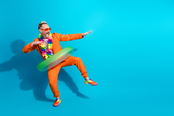 Fun spirited man in orange suit with tropical accessories posing against a vibrant blue background...