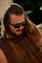 Portrait of a long haired bearded man in a brown t-shirt and sunglasses chilling in the hotel.