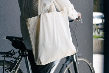 Woman holding eco bag or cotton tote bag in the city while riding a bike
