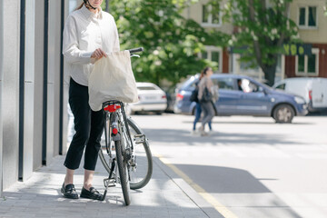 Fototapeta premium Woman holding eco bag or cotton tote bag in the city while riding a bike