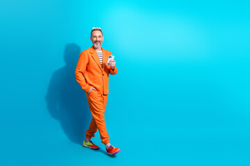 Mature gentlemen in a vibrant orange suit with phone against blue background, showcasing style and a friendly demeanor