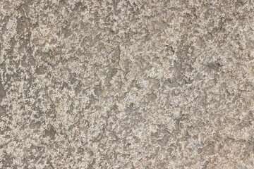 Close-up of rough beige-grey stone surface with visible relief. Empty background with natural unpolished stone texture.