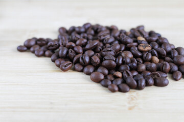 Scattered roasted coffee beans on a light wooden table create a rich, aromatic scene, inviting coffee lovers and enthusiasts to indulge in the essence of a perfect brew