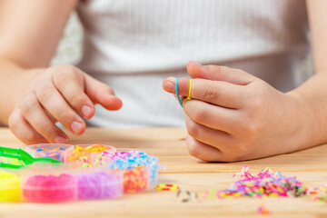 Hands of a girl weaving a bracelet with multi-colored rubber bands. Development of fine motor skills of fingers