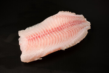 Fresh tilapia fillet on black background, top view.