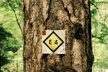 E4 European hiking trail marker on tree. Close-up of an E4 trail sign attached to a tree trunk in the forested region of Mount Olympus, Greece, guiding hikers.
