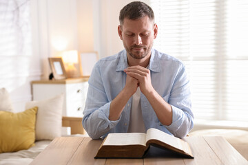Man with Bible praying at table indoors
