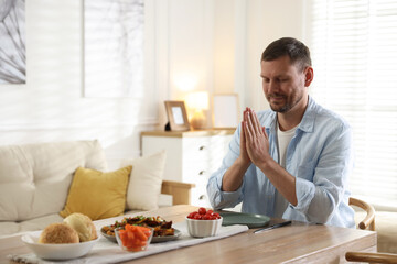 Man praying before dinner at table indoors. Space for text