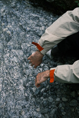 A person in a light jacket crouches by a cold, rocky stream in Mount Olympus, dipping hands near the flowing water.
