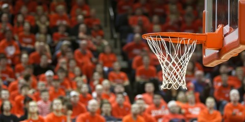 A basketball net is in the foreground of a crowd of people wearing red shirts