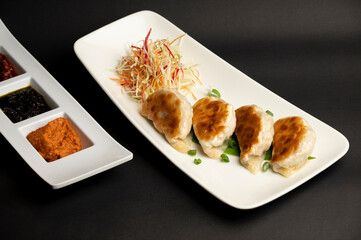 Juicy chicken dumplings served in a white plate with soy-vinegar sauce, garlic dip, and spicy dip, delicately steamed and styled for a rich, flavorful presentation on black background 