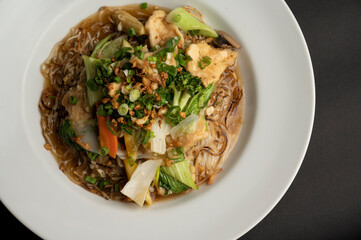 Top view of Pad Thai rice noodles with chicken and egg in a white plate, garnished with lime, crushed peanuts, spring onion, and sprouts, styled on a black background.