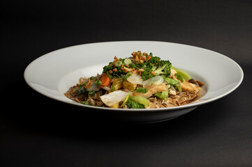 Pad Thai rice noodles with chicken and egg served in a white plate on black background, garnished with peanuts, lime, spring onion, and sprouts for a vibrant, traditional Thai dish.