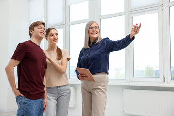 Smiling real estate agent with tablet showing apartment to couple indoors, low angle view