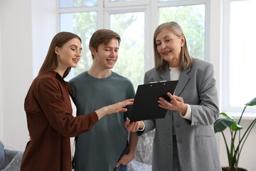 Smiling real estate agent with clipboard working with couple at home