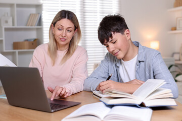 Mother helping her son with homework at table indoors