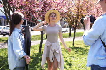 Professional photographers with reflector and camera near model during shooting outdoors on sunny...