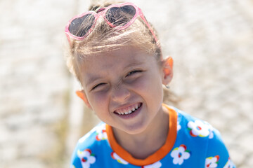 Happy little girl with long brown hair wearing a princess headband winking and smiling at the camera. Outdoor close-up portrait with soft natural light and a blurred background...