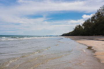Soft ocean waves gently lapping a long, sandy shore under a stunning sunset sky at Wanakon National Park, Thailand.