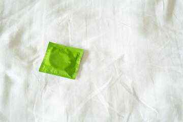 Unused condom lying on a rinkled white bedsheet.
