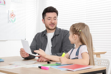 Teacher having lesson with little girl at desk indoors