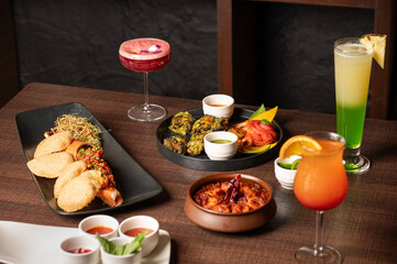 Kharda Chicken Tikka, Goan Lobster Recheado, and Prawns Balchao served with chutney, papad, and three vibrant cocktails on a table styled for an Indian coastal feast.

