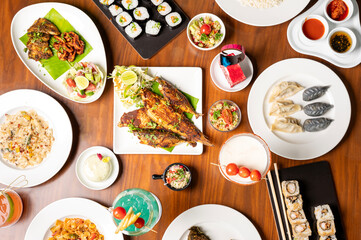 Top-down view of a diverse spread of dishes on a table, including fried mackerel, sushi, dim sum,...