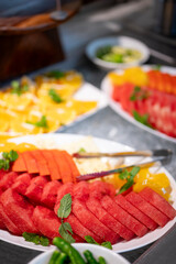 Close-up of a vibrant fruit salad plate at a buffet counter, featuring freshly cut watermelon, pineapple, and oranges arranged for a refreshing and healthy dining experience.