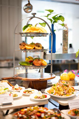 Foreground of gourmet non-vegetarian salads in small bowls with a vibrant stand of cut fruits and fresh vegetables in the background, styled at a hotel buffet counter.


