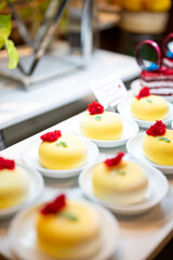 Close-up of classic round pineapple pastry topped with bright pineapple slice and cherry, layered with cream and sponge, displayed at a dessert counter in a bakery or hotel buffet.