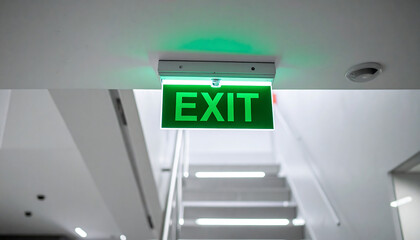 A realistic exit sign glowing in green, hanging from the ceiling above a stairwell