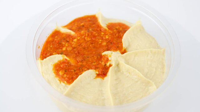 A top view of hummus sauce rotating on a white background. Showing the even distribution of red pepper paste on the creamy hummus.
