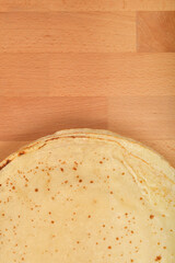 A top-down shot features a stack of freshly made, thin pancakes with golden-brown spots, resting on a light wooden surface