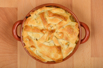 A top-down shot showcases a golden-brown, freshly baked chicken pot pie in a rustic ceramic dish with golden brown pastry crust