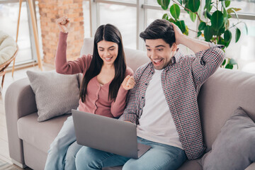 Obraz premium Young Couple Celebrating Success Together on the Couch with a Laptop in a Bright and Cozy Living Room Interior