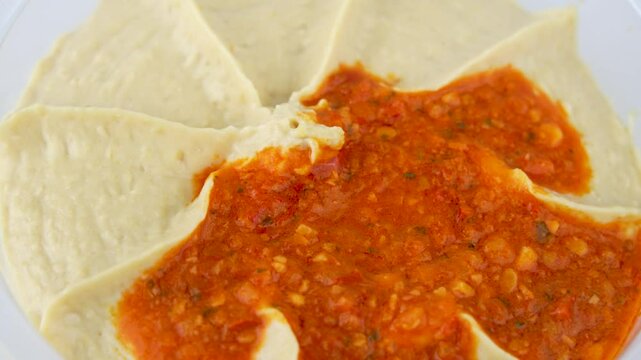 A close-up view from above of the rotating hummus dip. Showing the even distribution of red pepper paste on the creamy hummus.