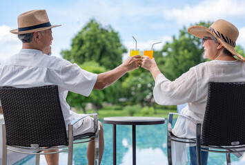 happy senior couple enjoy talking with freshy drink on table,sitting,relaxing by the pool,elderly people travel destination tropical resort and spa on summertime