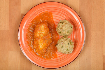 Overhead shot shows a plate with chicken paprikash and two bread dumplings on a wooden surface