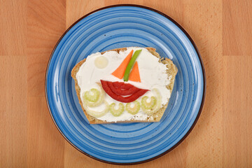 Creatively decorated cream cheese and vegetable sandwich on a blue plate, shaped to resemble a boat...