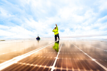 A technician in safety gear inspects solar panels on a metal rooftop, holding a tool. The scene...