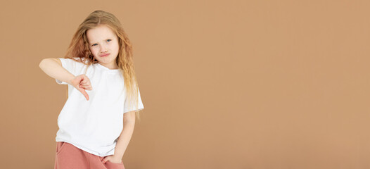 Young sad displeased unhappy girl wear white t-shirt showing thumb down dislike gesture isolated on...