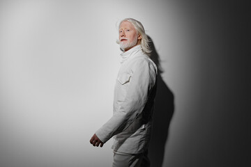 Portrait of a person with long white hair dressed in a white outfit, set against a gradient gray...