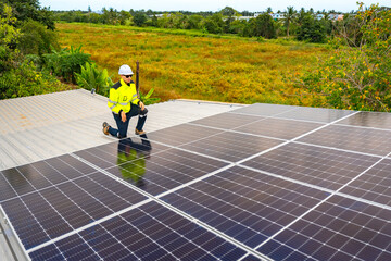 A technician in safety gear inspects solar panels on a metal rooftop, holding a tool. The scene...