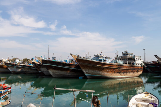 Traditional wooden dhows docked in the calm waters of Bushehr harbor, showcasing the maritime heritage of southern Iran under a clear sky.